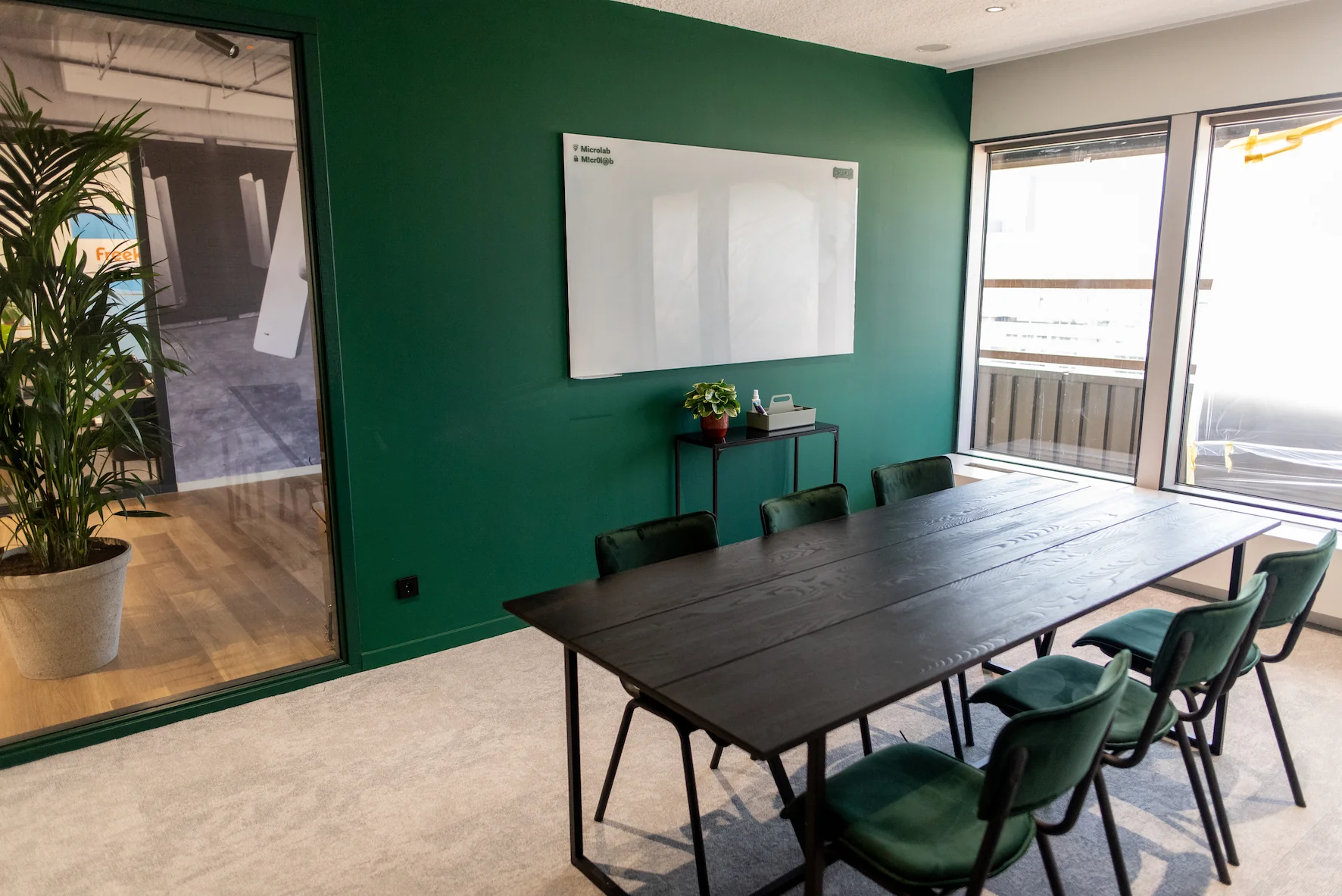 Vergaderruimte aan de Aert van Nesstraat met donkergroene muur, zwarte tafel, zes stoelen en een whiteboard.